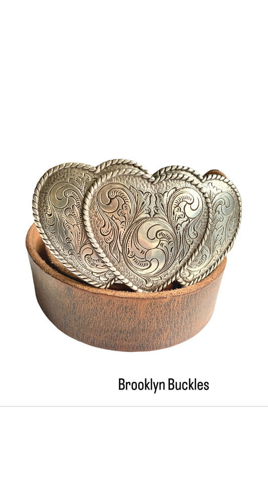 Three ornate hearts belt buckle attached to a brown belt coiled on white background with branding text Brooklyn Buckles.