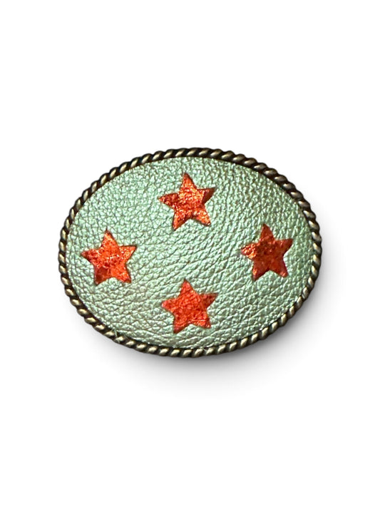 An oval leather belt buckle featuring a light mint green metallic design with four orange metallic star cutouts with a rope trim. 