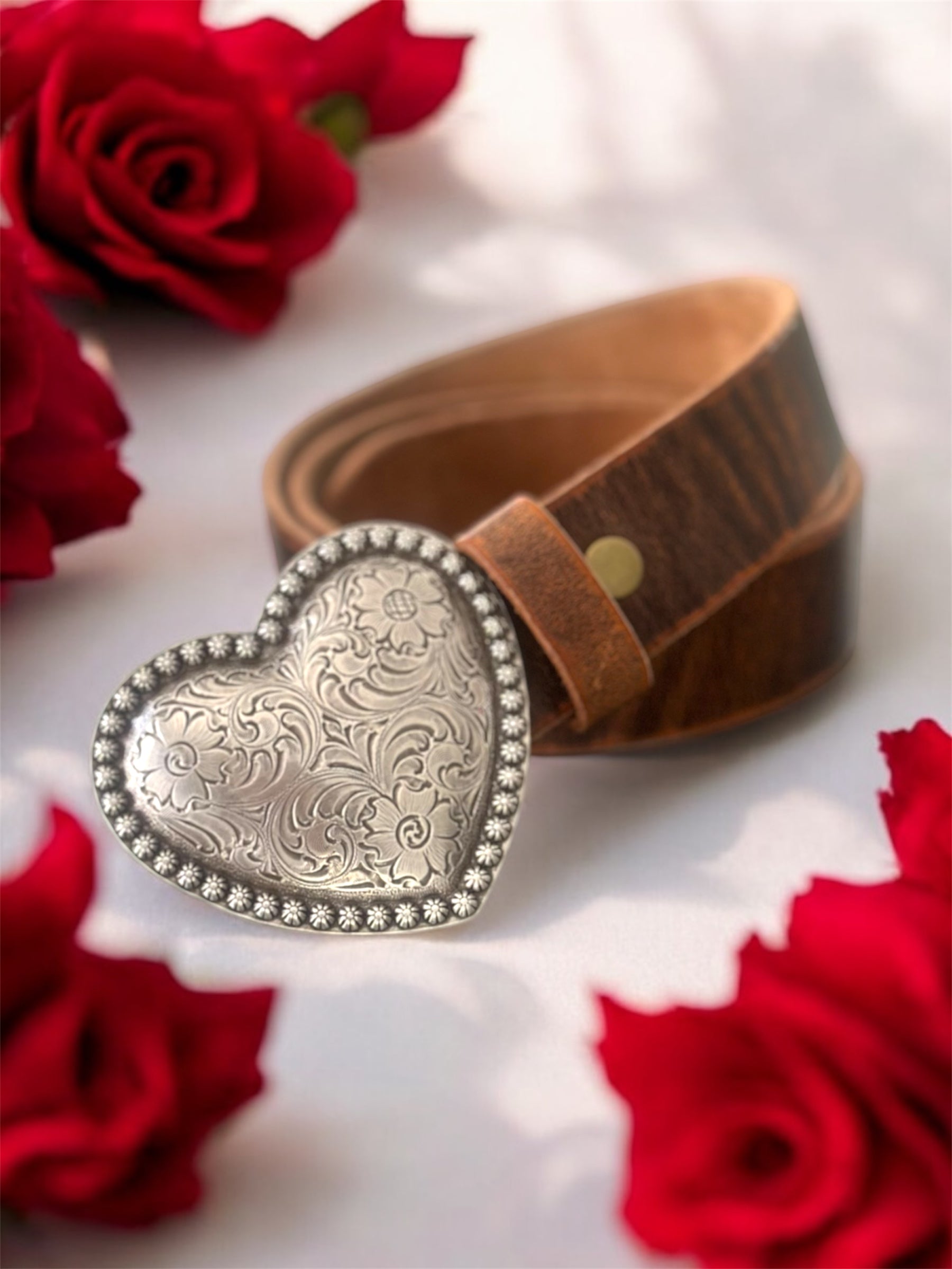 Brown leather belt with a silver heart-shaped buckle on a white background with red roses.